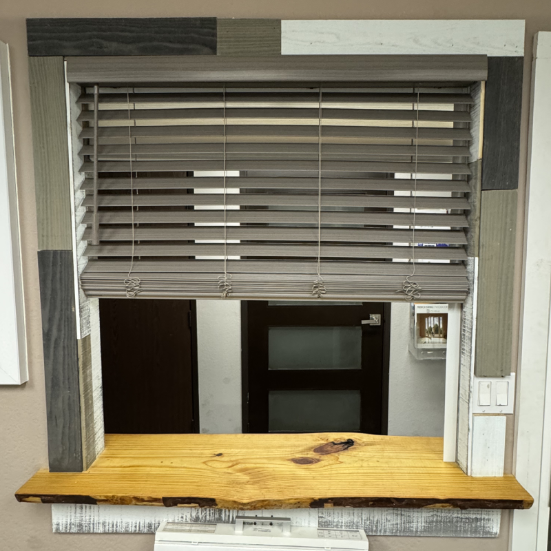 Faux wood blind by Norman A wooden-framed window with horizontal blinds, featuring a variety of textured wood accents in muted colors and a wooden sill below.